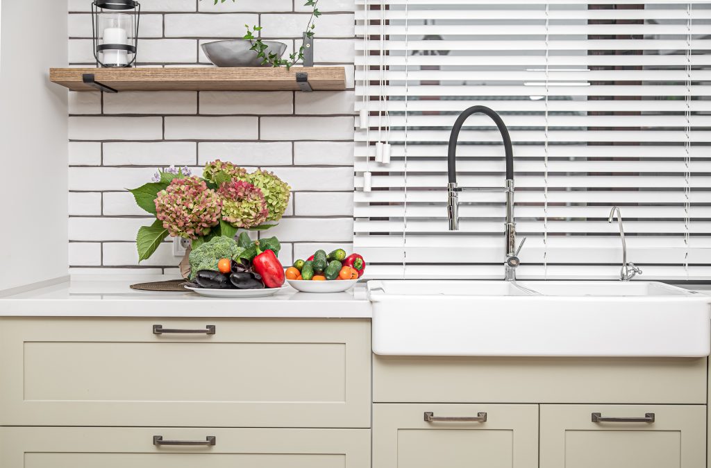 White kitchen cabinets with metal handles on the doors near the washbasin with a bouquet of flowers and a plate of vegetables.