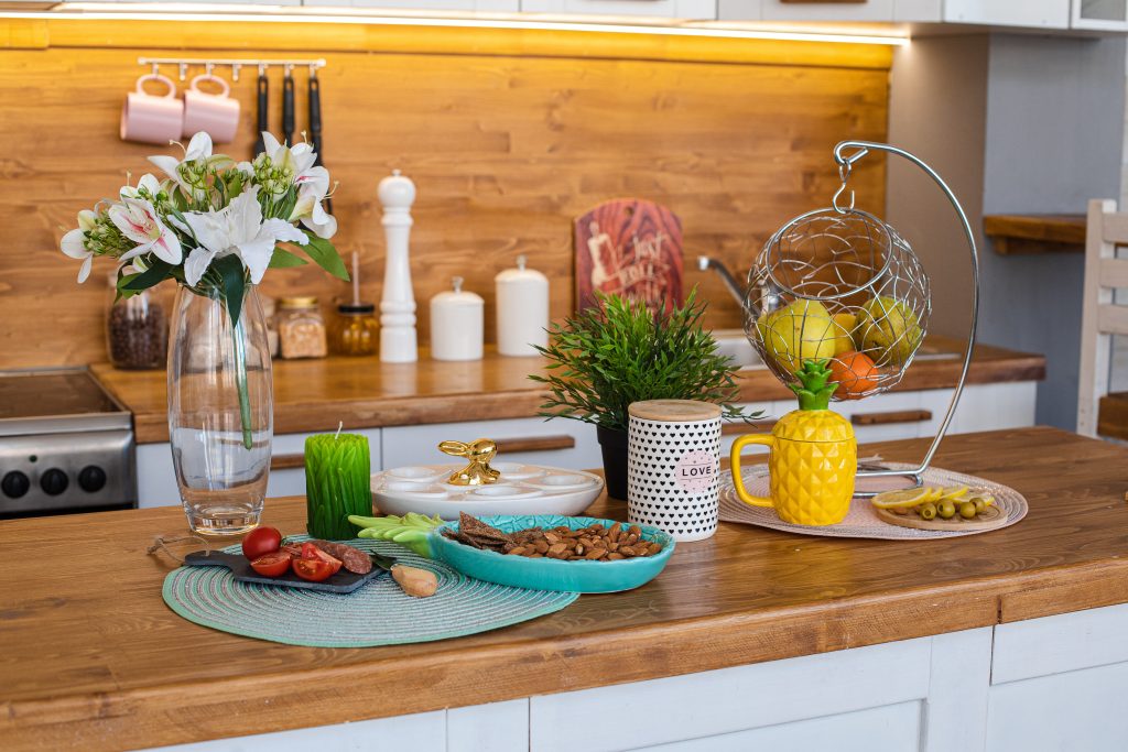 View over wooden counter set with snacks, lily flowers, fresh fruit in basket.