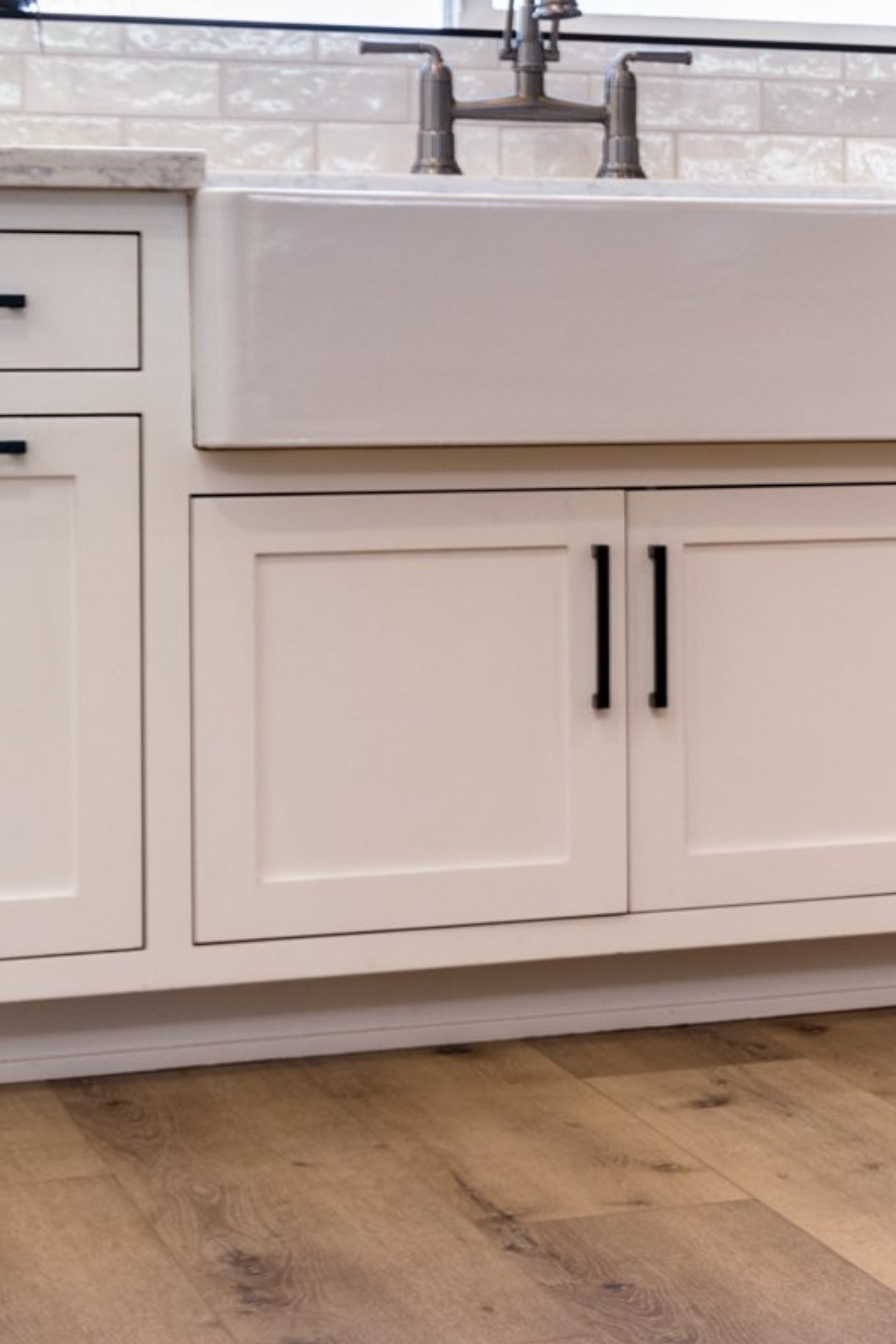 white kitchen cabinets with farmhouse curtain style sink and a white toe kick plate molding underneath