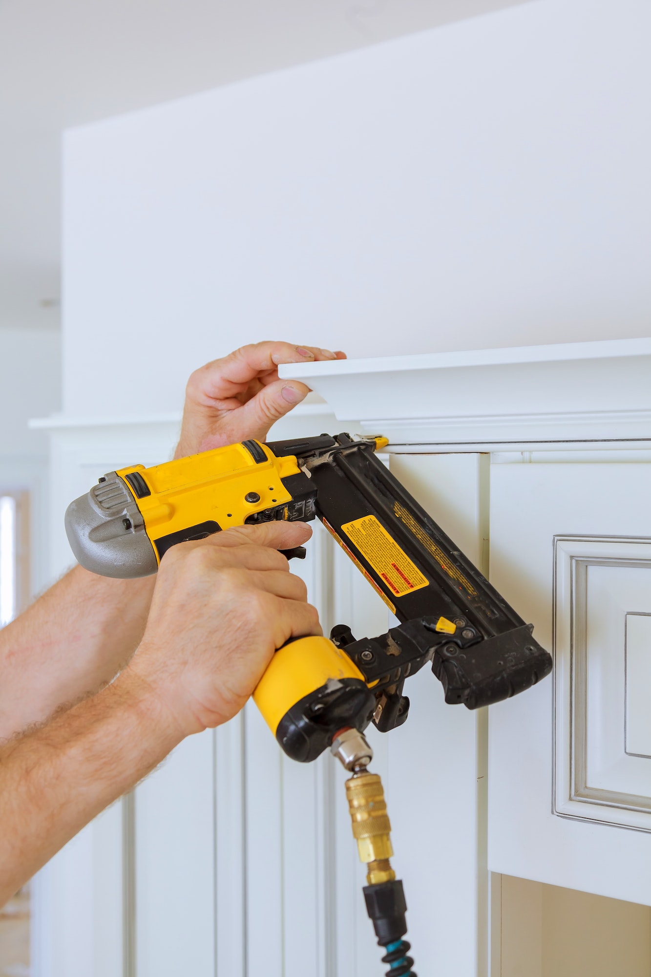 Carpenter brad using nail gun to Crown Moulding on kitchen cabinets framing trim