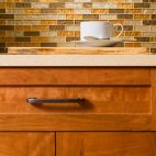 High quality cherry wood cabinets with bronze cabinet hardware & glass tile mosaic backsplash in contemporary upscale home kitchen