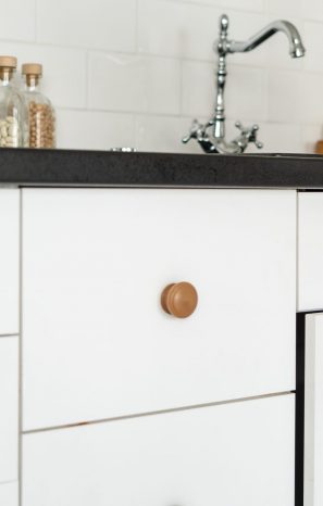 Cropped view of woman hand open cabinet door, pulling handle, standing at white modern kitchen in house with drawers under countertop