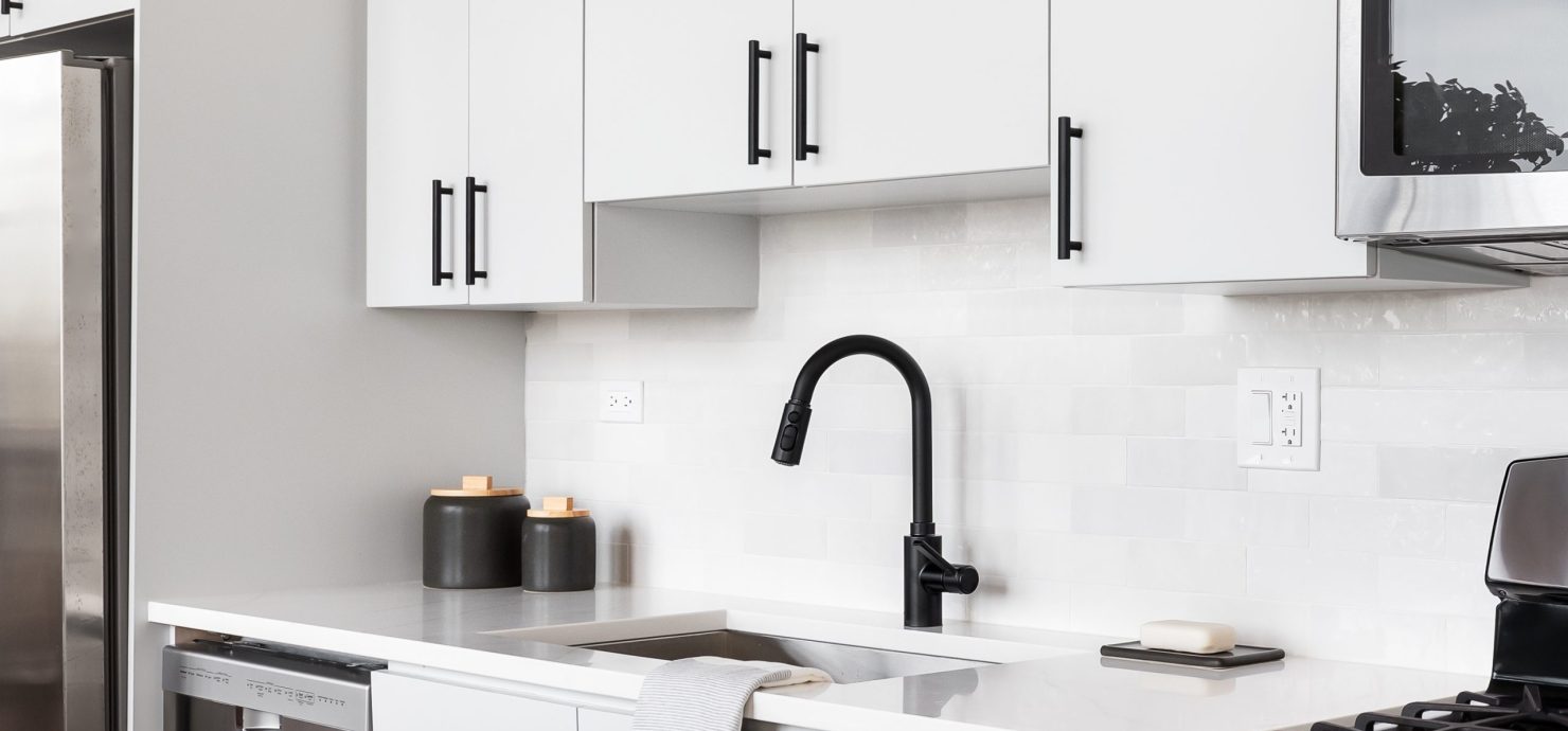 A beautiful white kitchen detail shot with a tiled backsplash, white cabinets, stainless steel appliances, and black hardware and faucet.