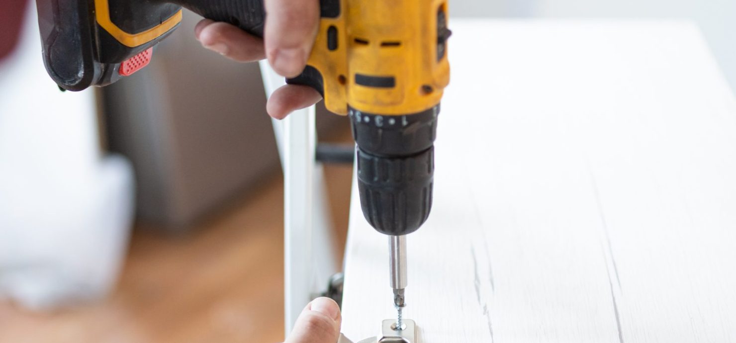 Close up of man assembling furniture by using cordless screwdriver