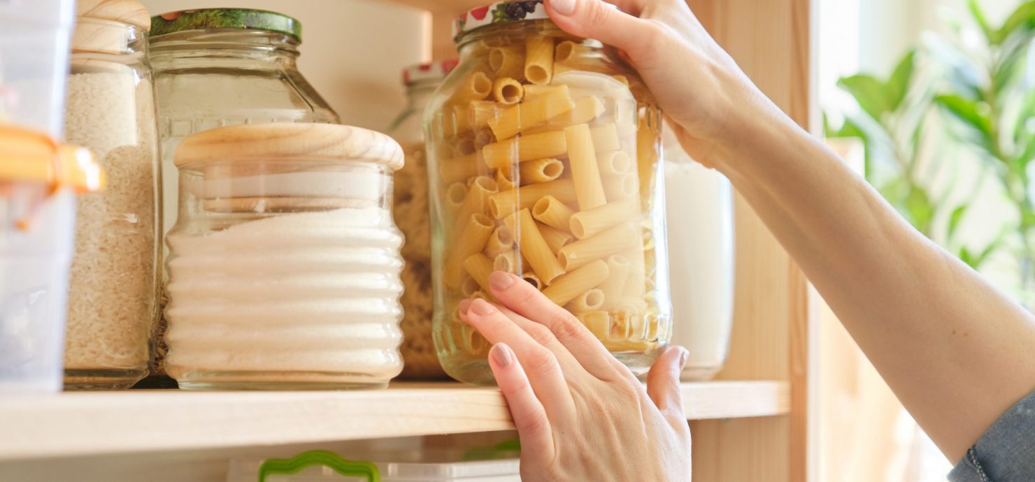 Food products in the kitchen storing ingredients in pantry. Woman taking jar of pasta