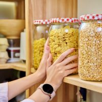 Storage of food in kitchen in pantry, woman's hands with a can of corn flakes. Cereals, food in jars containers on wooden rack. Cooking at home, stocking food, household