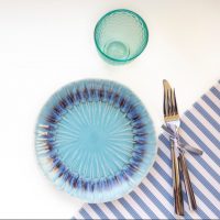 Table set in marine style - empty plates in shape of fish and blue sea, glass,fork and knife on stri