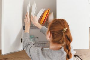 Opening kitchen cabinet door, woman putting plates into it.