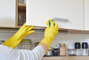 woman in yellow gloves washes the door in kitchen cabinet